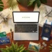 Laptop displaying 'EXPLORE' surrounded by travel essentials and maps